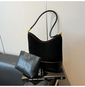 Détail du sac cabas en daim noir et de sa pochette assortie sur un canapé en cuir