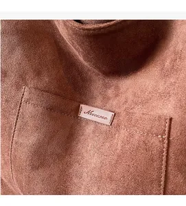 Close-up of brown suede fabric texture and stitched leather brand label on the tote bag