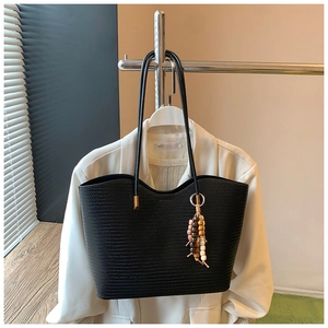 Détail d'un sac cabas noir tressé avec pendentif en perles sur la bandoulière