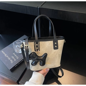 Detail view of a beige canvas bucket bag with black leather trim and a puppy charm
