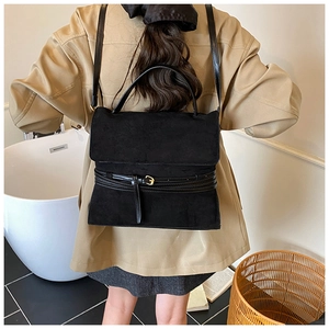 Detalle de bolso de ante negro mate con hebilla cuadrada dorada usado por una modelo