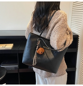 Detail of black faux leather tote bag with gold logo plate and cute teddy bear charm