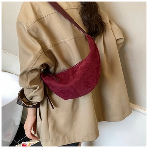 Model wearing a burgundy suede half-moon bag over a trench coat for autumn style