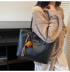 Detailed view of black tote bag with textured faux leather and teddy bear charm