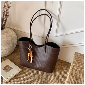 Détail d'un sac cabas tressé marron foncé avec pompon en perles et fines bandoulières