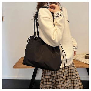 Detail of minimalist black nylon tote bag with drawstring closure on model