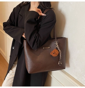 Detail of dark brown tote bag with leather texture and cute teddy bear charm