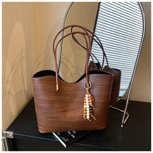 Détail du sac cabas tissé marron foncé avec de longues bandoulières et un charm perlé