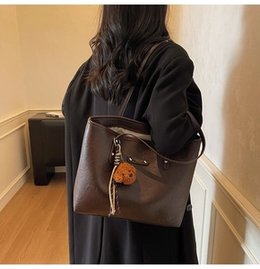 Detail of deep brown retro tote bag with golden plaque and teddy bear charm on shoulder