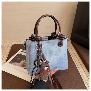 Dettaglio borsa tote in denim azzurro con manici intrecciati e ciondolo a orsetto