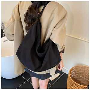 Détail du sac cabas en toile noire avec perles en bois sur la bandoulière, porté à l'épaule