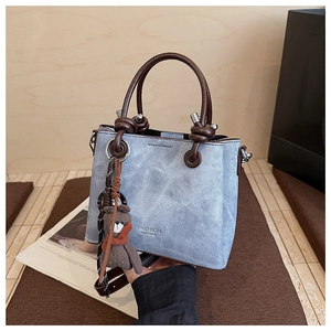 Dettaglio della borsa tote in denim azzurro con manici tondi marroni e ciondolo a orso