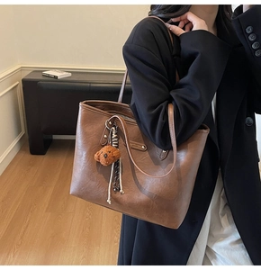 Brown leather tote bag featuring a cute plush dog pendant and textured woven rope details