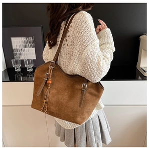 Detail of a large brown suede tote bag featuring a tassel charm and adjustable strap