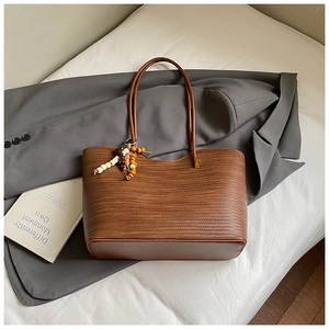 Détail du sac cabas marron tissé avec pompon en perles de bois colorées sur un blazer gris