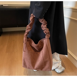 Detail of a brown suede tote bag featuring a pleated handle and functional front pocket