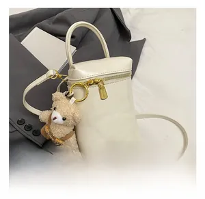Détail du mini sac à main crème avec fermeture éclair dorée et breloque ours en peluche