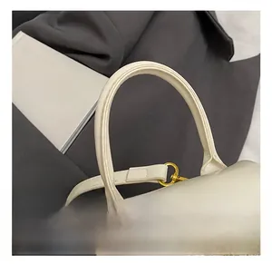 Détail d'un sac à main beige montrant l'anse rigide et les boucles en métal doré