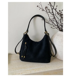 Detail of black frosted suede shoulder bag featuring gold hardware and double tassels
