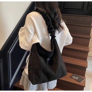 Detail of black suede tote bag with wide pleated shoulder strap in real-life use