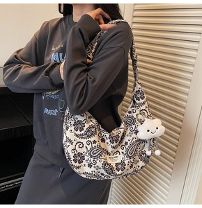 Detail einer bedruckten Halbmond-Tasche mit breitem Gurt und Plüschanhänger am Modell