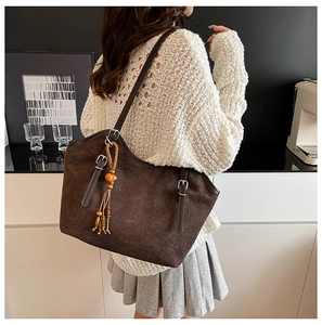 Detail of dark brown matte tote bag with fringe charm and leather strap accents