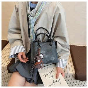 Dettaglio della borsa a secchiello grigia in pelle vintage con manico nero e orsetto