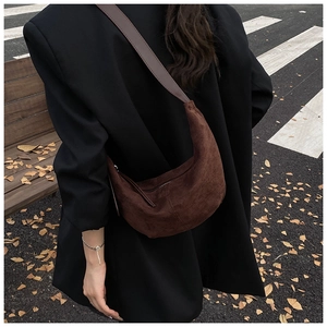 Brown suede crescent bag shown from side profile on shoulder in a cozy autumn street setting