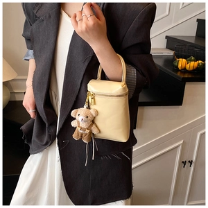 Gros plan d'un mini sac à main crème avec fermeture éclair dorée et breloque ours en peluche