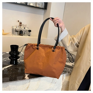 Detail of caramel nylon tote bag with drawstring closure and black handles in cafe setting
