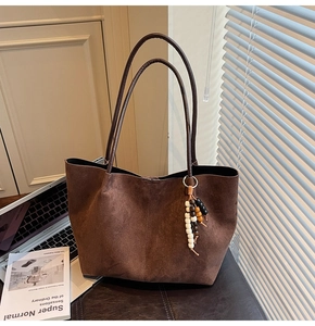 Détail du cabas en daim marron foncé avec pendentif en perles sur un tabouret