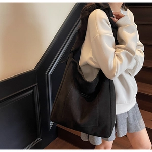 Large black suede tote bag shown on shoulder, matching white sweatshirt and gray skirt