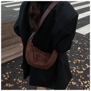 Detail of a deep brown frosted leather crescent bag shown on a model in an autumn street