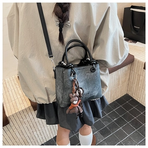 Vista dettagliata di una borsa tote grigia vintage con logo fashion e ciondolo a orso
