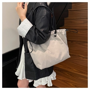 Detail of grey oversized tote bag with drawstring closure and slim black straps on model