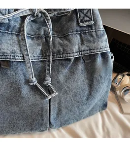 Close-up of blue denim tote bag showing wash texture, drawstrings, and detailed stitching