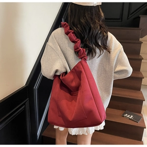 Detail of burgundy canvas tote bag featuring pleated wide shoulder strap and front pocket