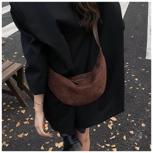 Close-up of a vintage brown suede crescent bag with zipper detail on a leather strap