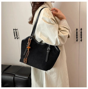Detail of black suede tote bag featuring a traditional ethnic wooden bead tassel charm