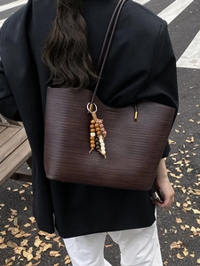 Grand sac cabas tressé marron foncé avec pompon en perles porté par une femme en tailleur