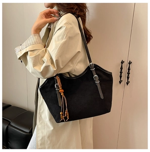 Side view of black matte suede tote bag with wooden bead tassel on a model in a trench coat