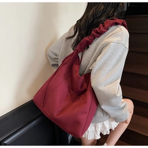 Detail of burgundy canvas tote bag featuring wide pleated cloud-style shoulder strap