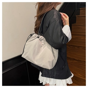 Detail of grey nylon drawstring tote bag with black leather straps worn by a model