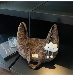 Nahaufnahme einer braun gemusterten Halbmond-Tasche mit süßem Wolken-Anhänger im Regal