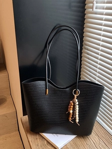 Grand sac cabas noir tissé avec pompon en perles de bois sur un banc en bois