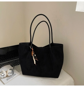Grand sac cabas en daim noir avec franges de perles colorées sur un bureau épuré