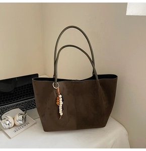 Detail einer großen braunen Wildleder-Tote Bag mit Perlenanhänger auf dem Schreibtisch