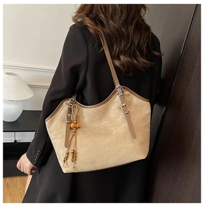 Detail of a large beige frosted tote bag featuring adjustable brown straps and wooden bead charm