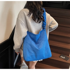 Detail of blue corduroy tote bag with wide pleated strap and large front pocket