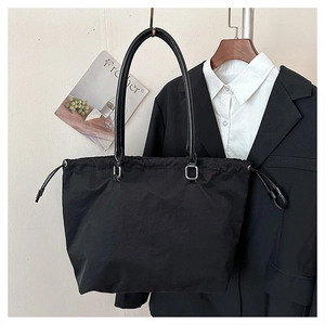 Detail of black drawstring tote bag with silver metal buckles and sleek nylon texture